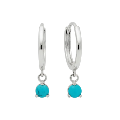 Qutahia Jewelry 14k solid gold huggie earrings with dangling turquoise gemstones in a claw setting.